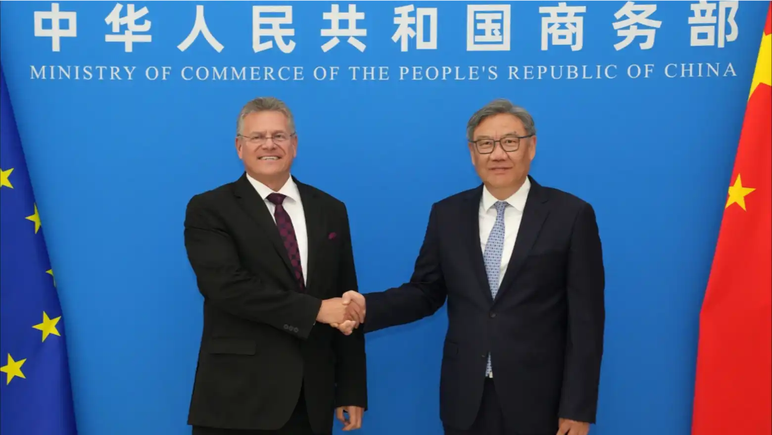 EU and Chinese trade officials shake hands in front of flags at a meeting in Beijing