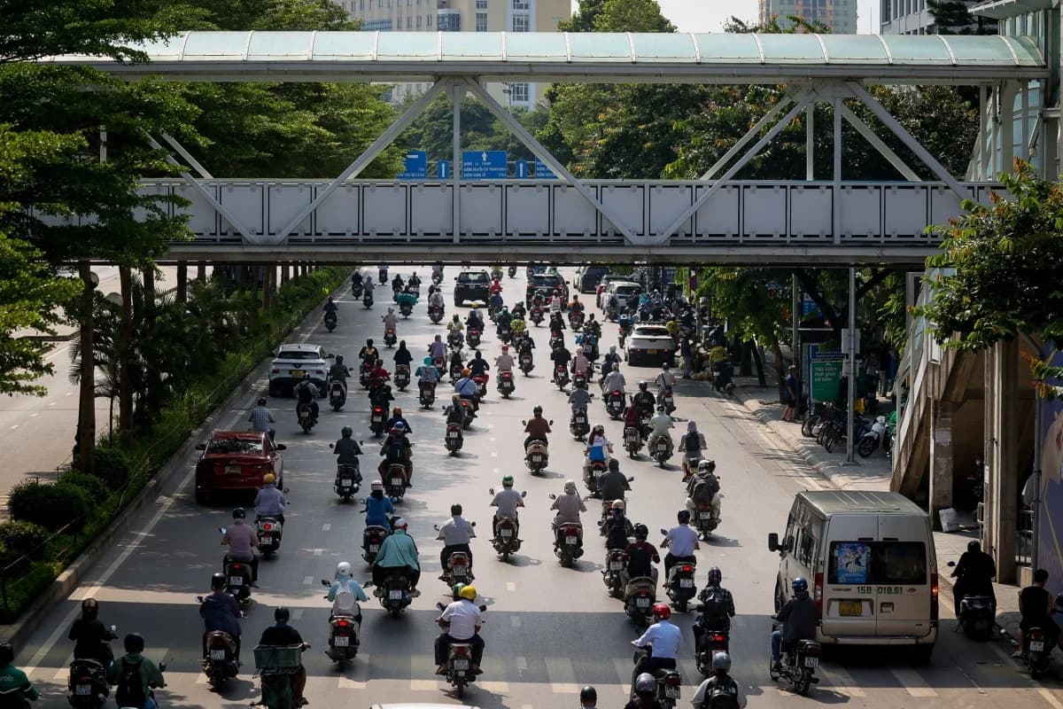 Heavy motorbike traffic flows beneath a pedestrian overpass on a street in Vietnam