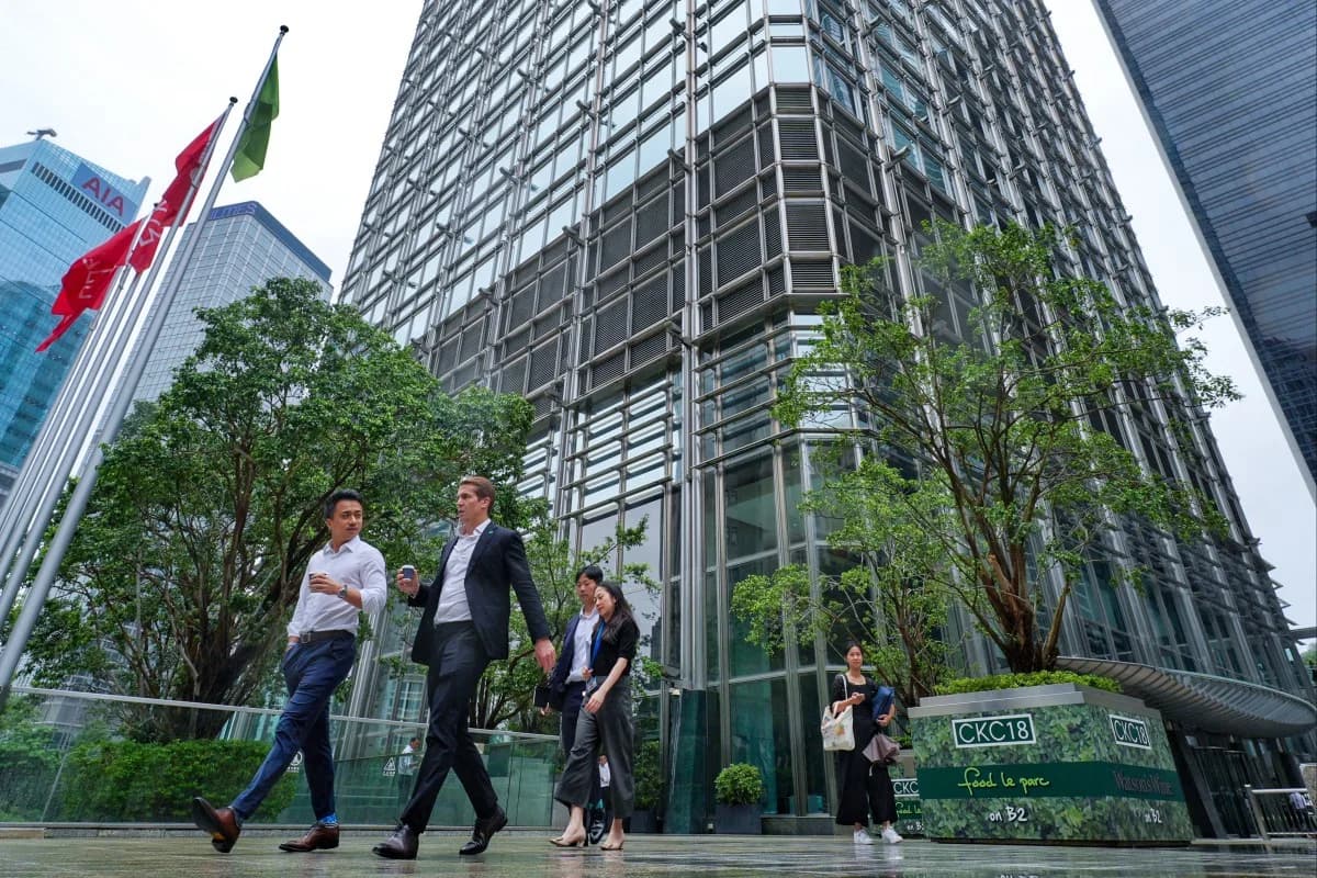 Office workers walk past a glass office tower in a Hong Kong business district